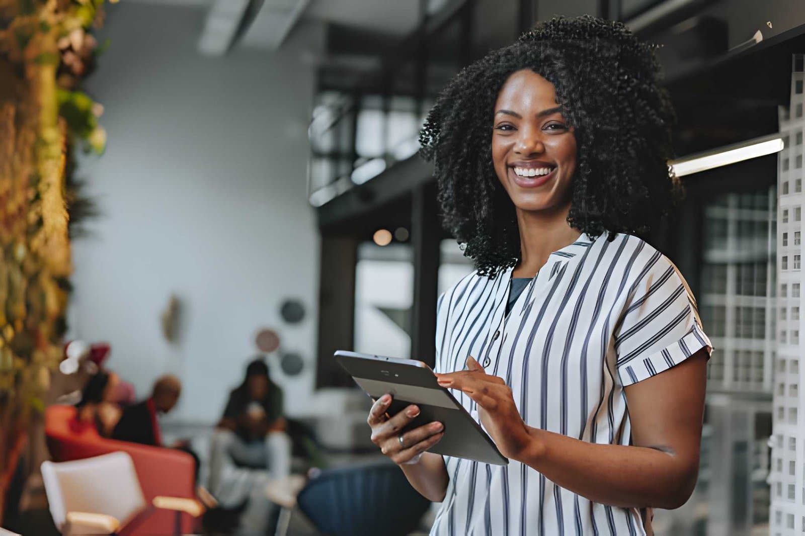 A smiling business owner holding a tablet in a bright open-plan office